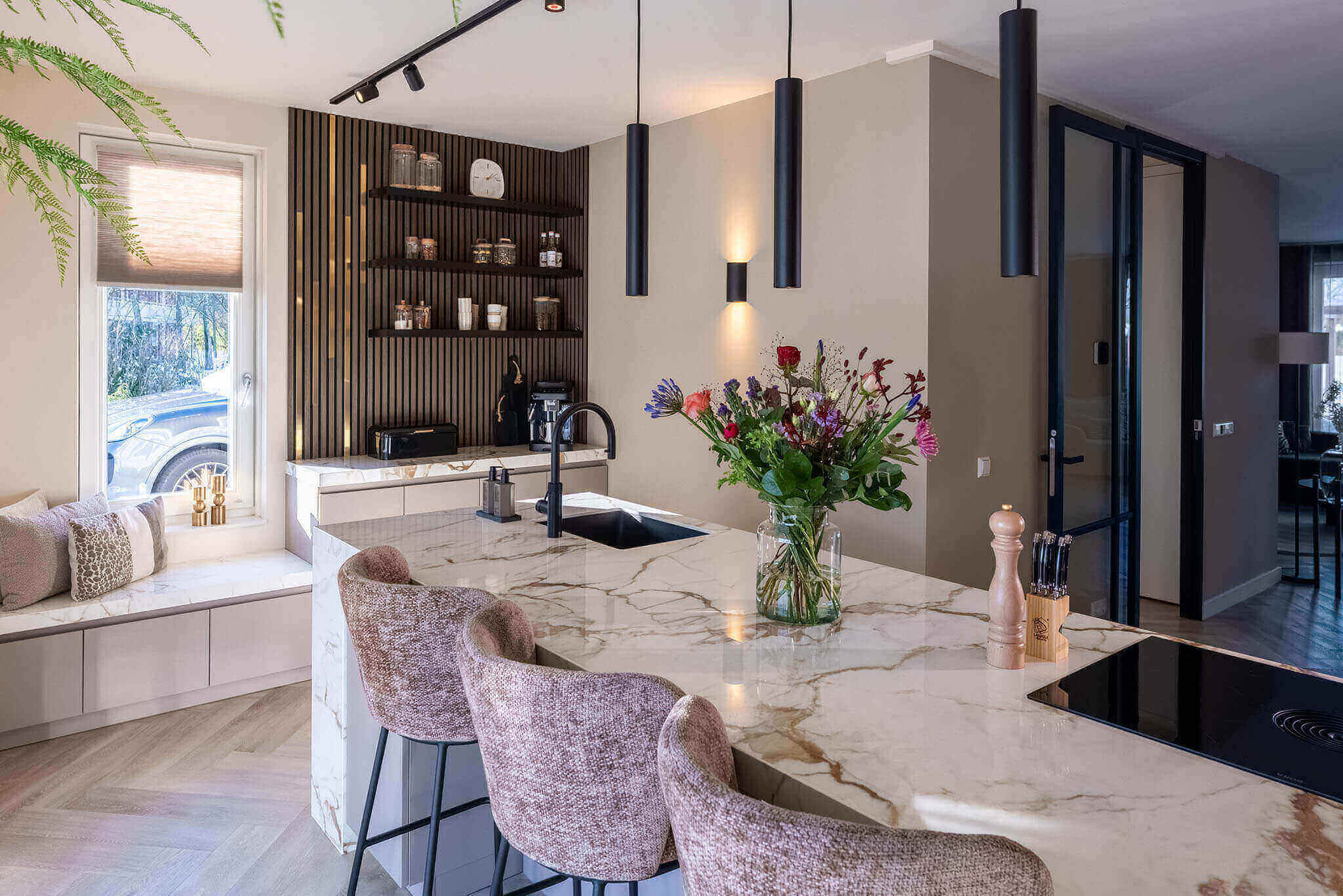 Luxe Tieleman-keuken met een licht marmeren kookeiland en roze barstoelen