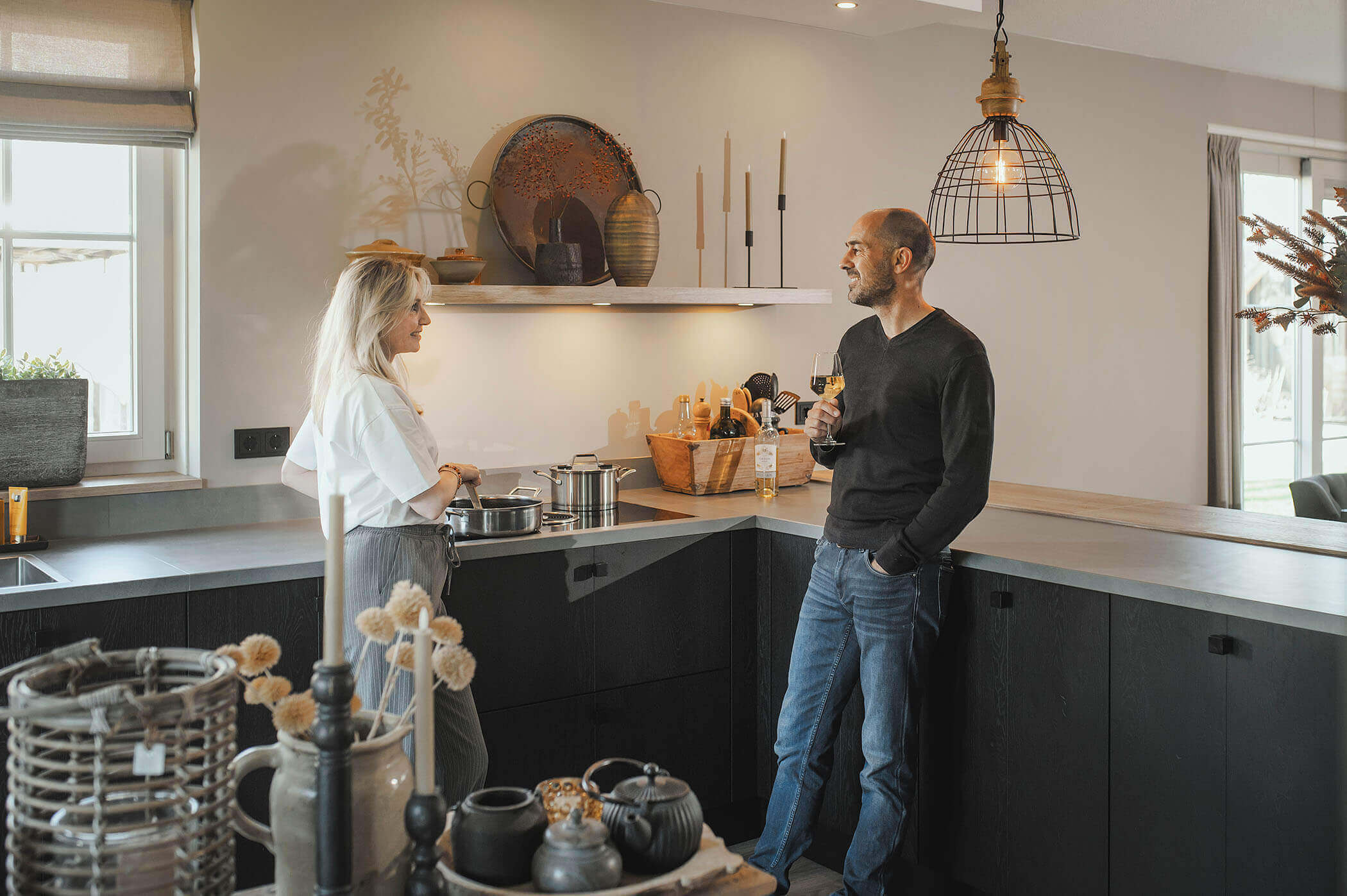 Een stel geniet van een glas wijn in een Tieleman-keuken van het merk Keller met een hoekopstelling en keukeneiland