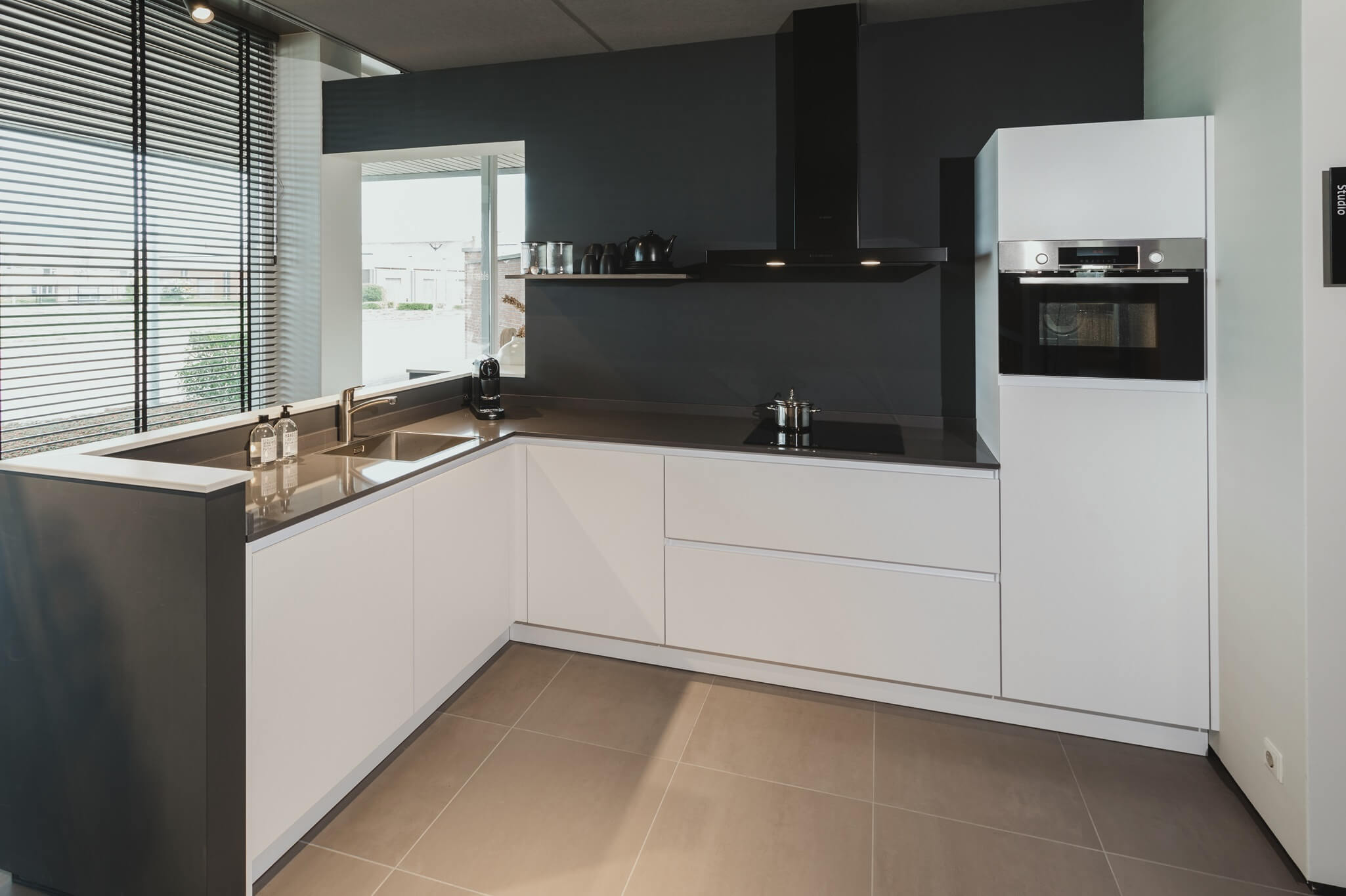 Moderne witte keuken met zwart blad en strakke afwerking, voorzien van ingebouwde oven en inductiekookplaat