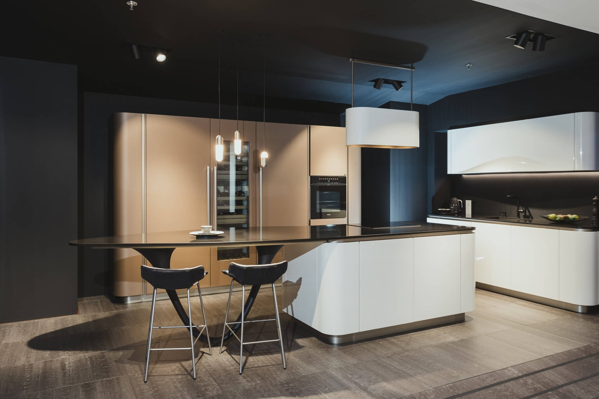 Ruime, moderne keuken met strakke witte kasten, een groot zwart composiet werkblad en een opvallend eiland met eetbar.