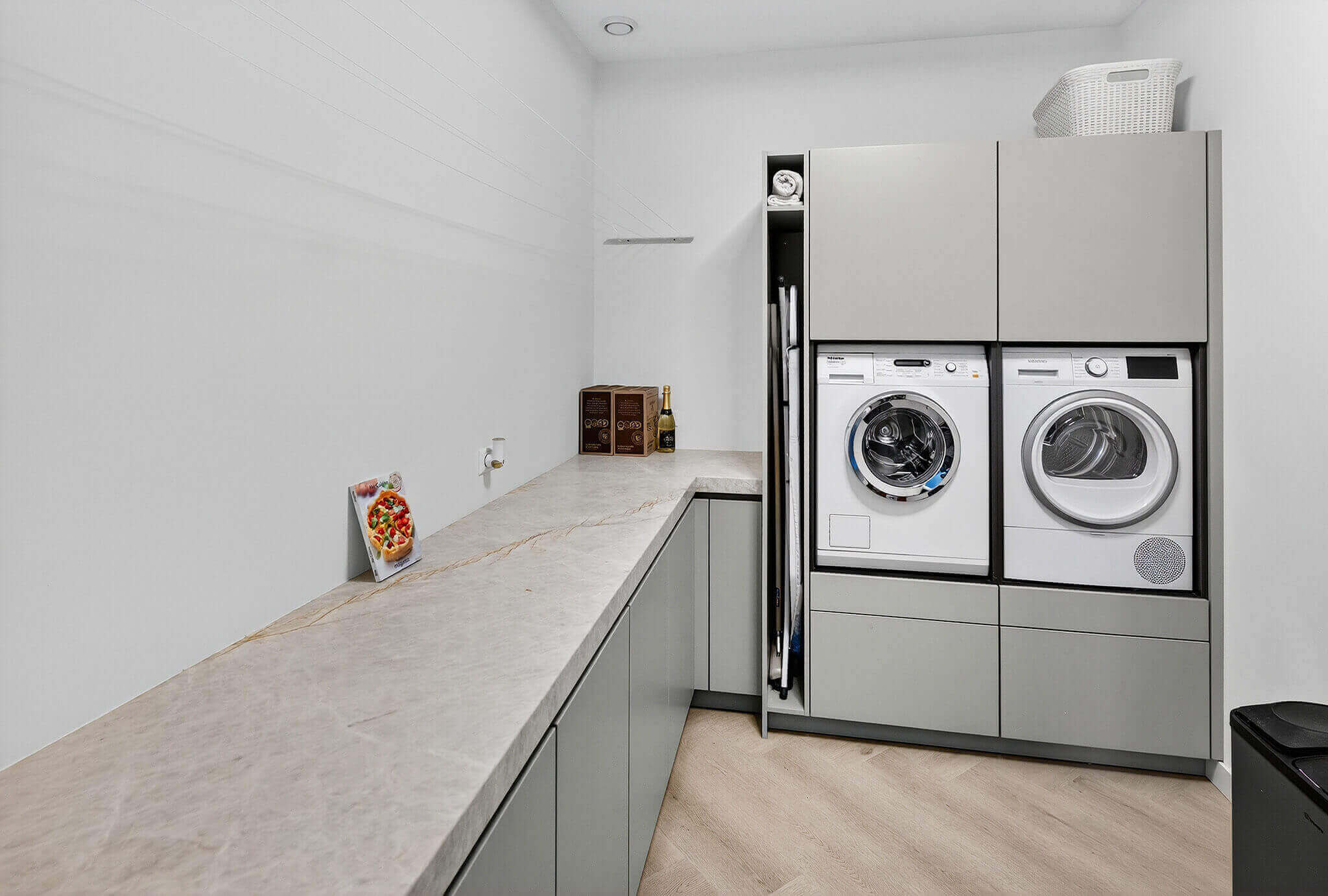 In deze handige bijkeuken is gekozen voor dezelfde grijze kasten en hetzelfde stenen werkblad als in de hoofdkeuken van Tieleman Keukens.