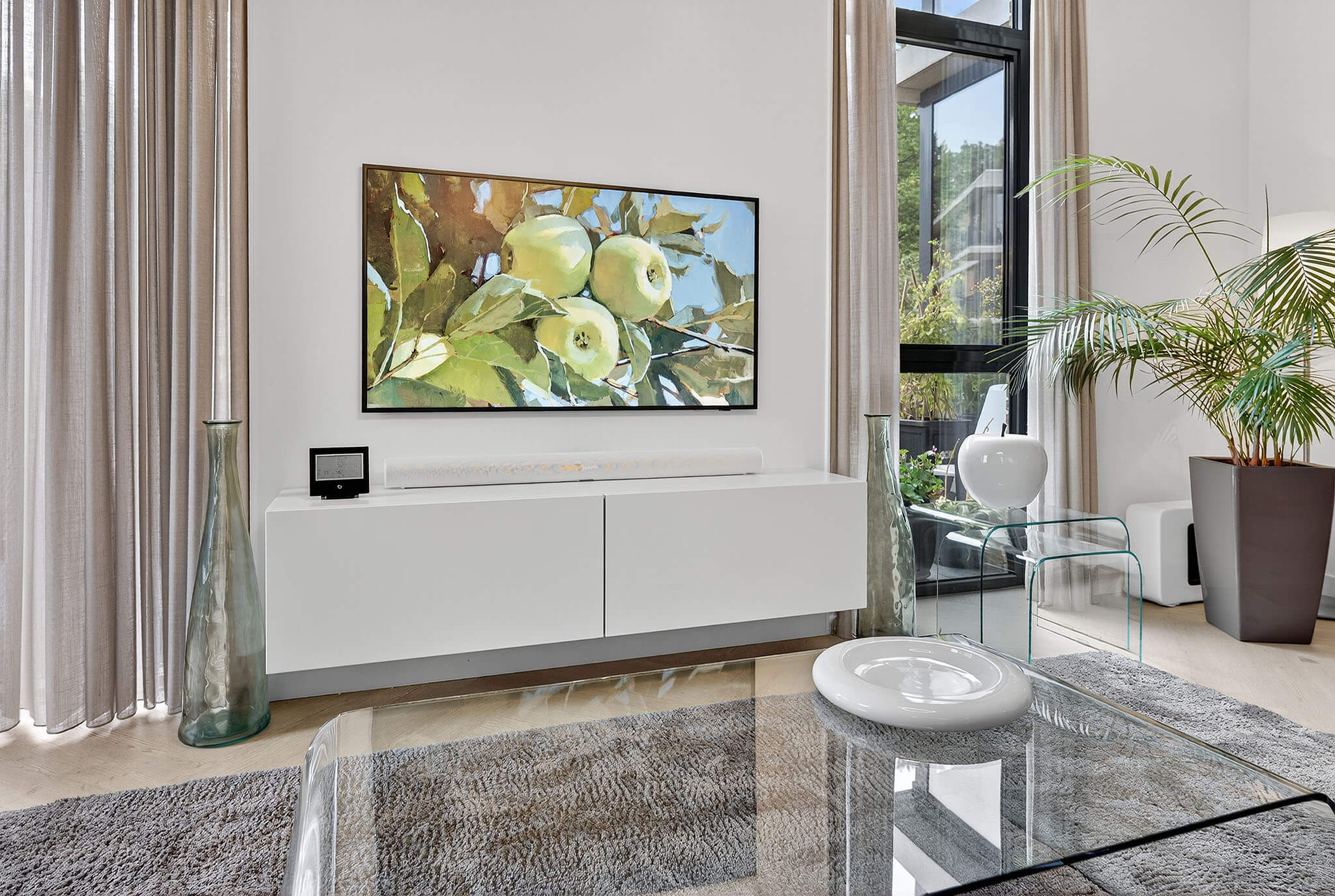 Een laag en strak wit meubel onder de televisie waarbij alle snoeren en apparaten netjes uit het zicht zijn geplaatst.