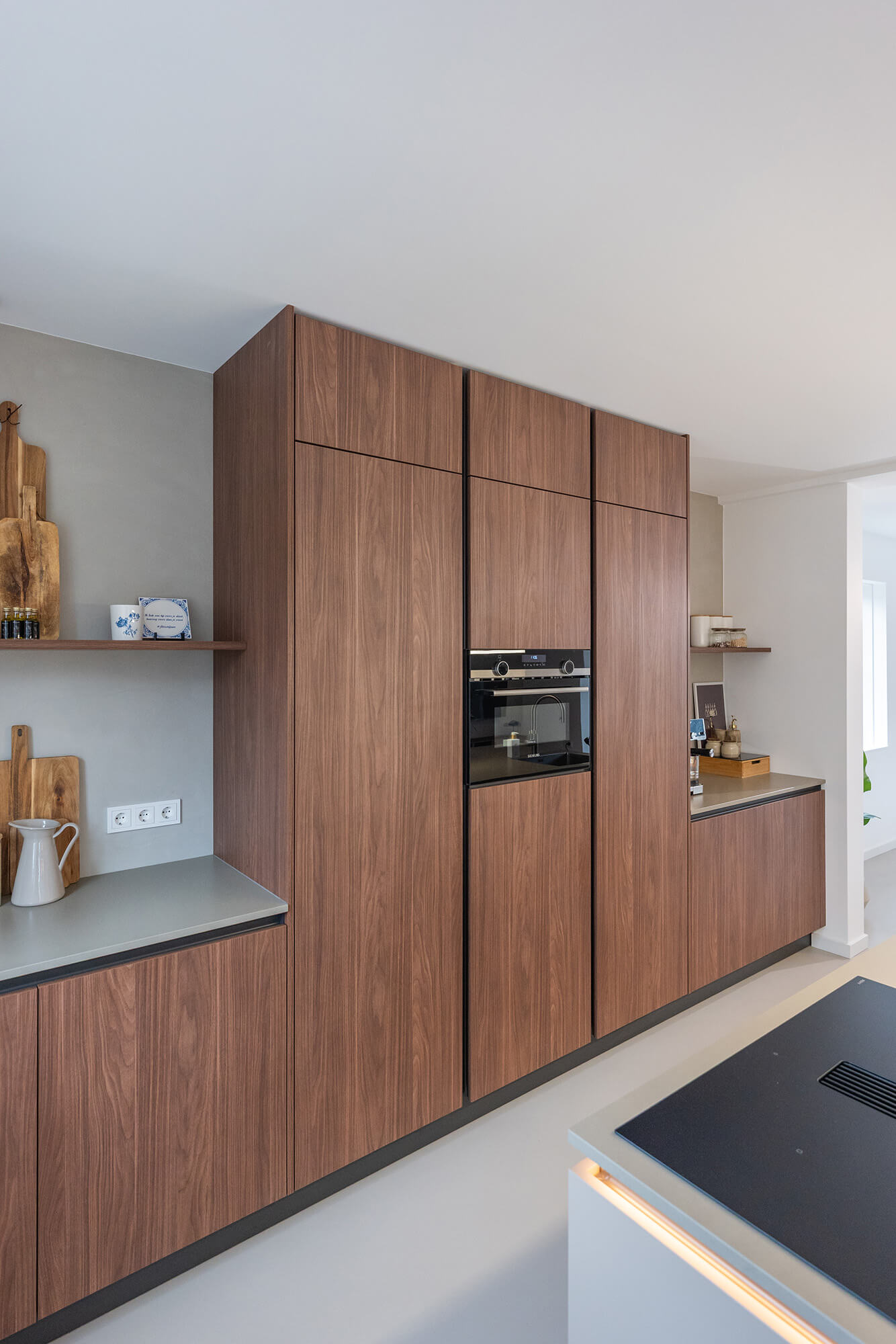 Warme houten kastenwand van een Tieleman-keuken met een ingebouwde oven en een sfeervolle nis voor accessoires.