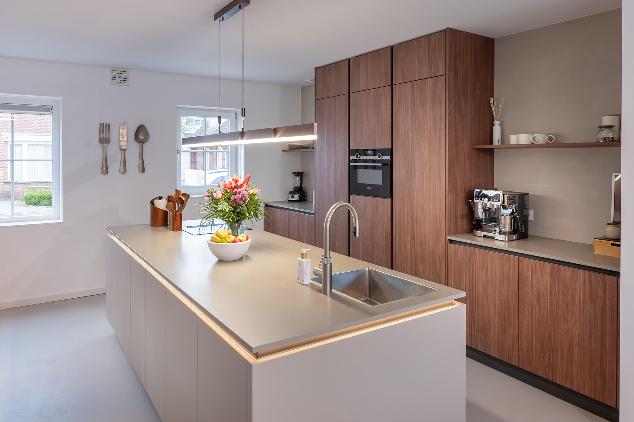 Luxe kookeiland van een Tieleman-keuken met verlichte greeplijsten en een lichtgrijs composieten aanrechtblad van Dekker.