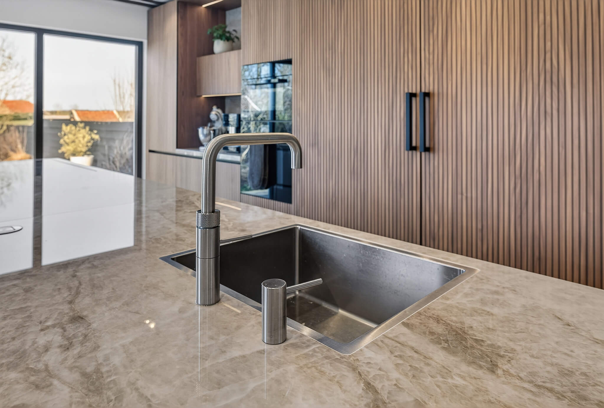 Keukeneiland met een marmeren Dekton Taga Xgloss aanrechtblad en een ingebouwde Quooker kraan.